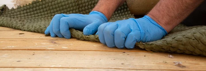 Hände mit Handschuhen entfernen Teppich von Holzboden